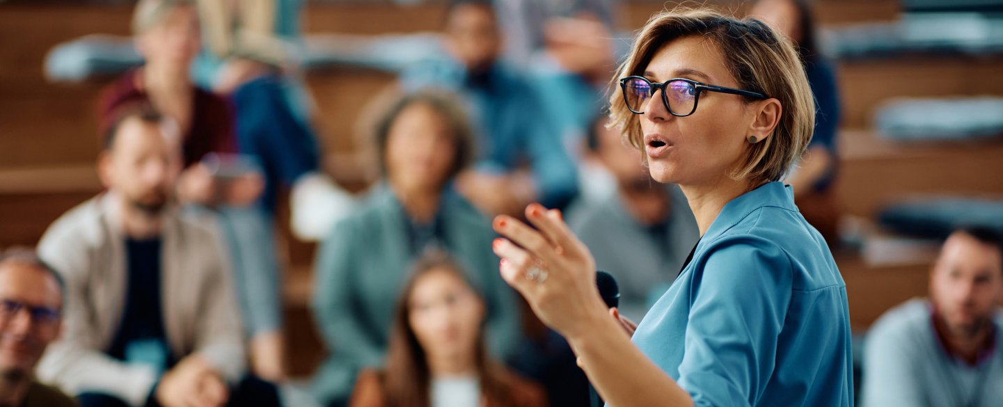 Woman in blue shirt and black glasses giving a speech