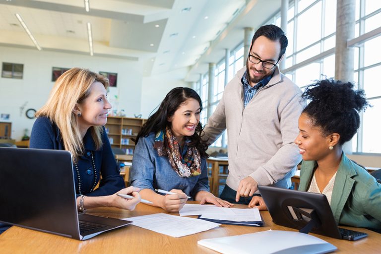 People smiling in a brightly lit office or library reviewing documents