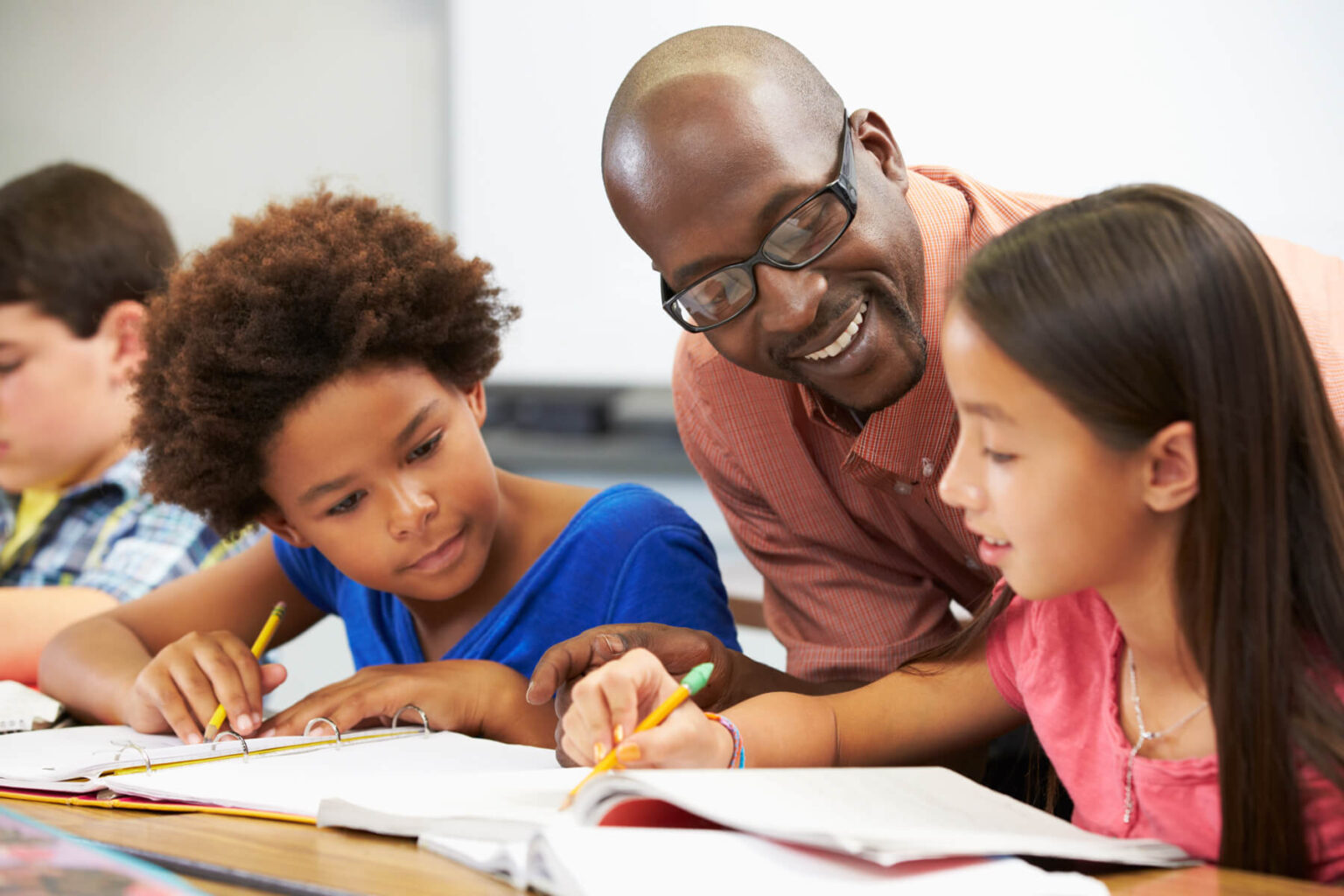 Photo of teacher leaning over the shoulder of young students working on homework or an assignment
